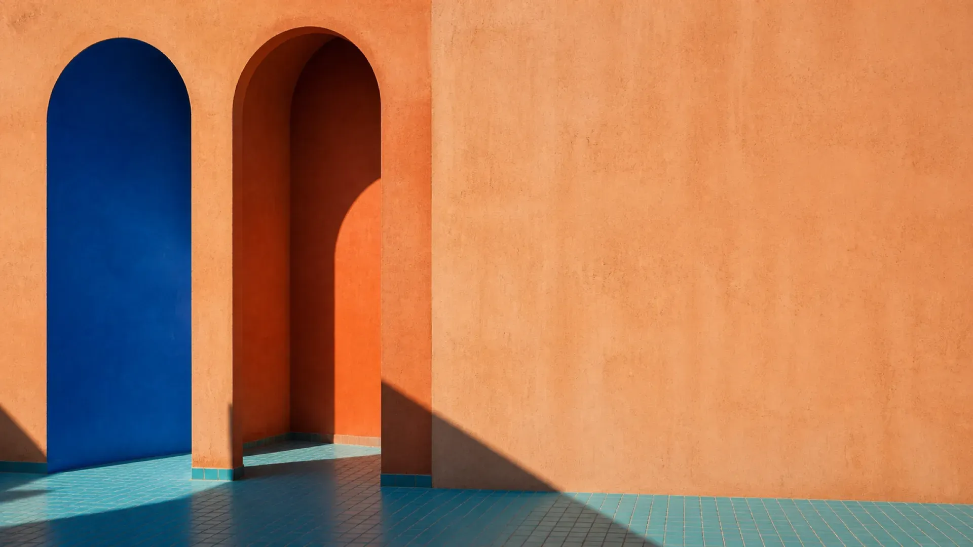 Two archways side by side, one cobalt blue and one terracotta, casting overlapping shadows