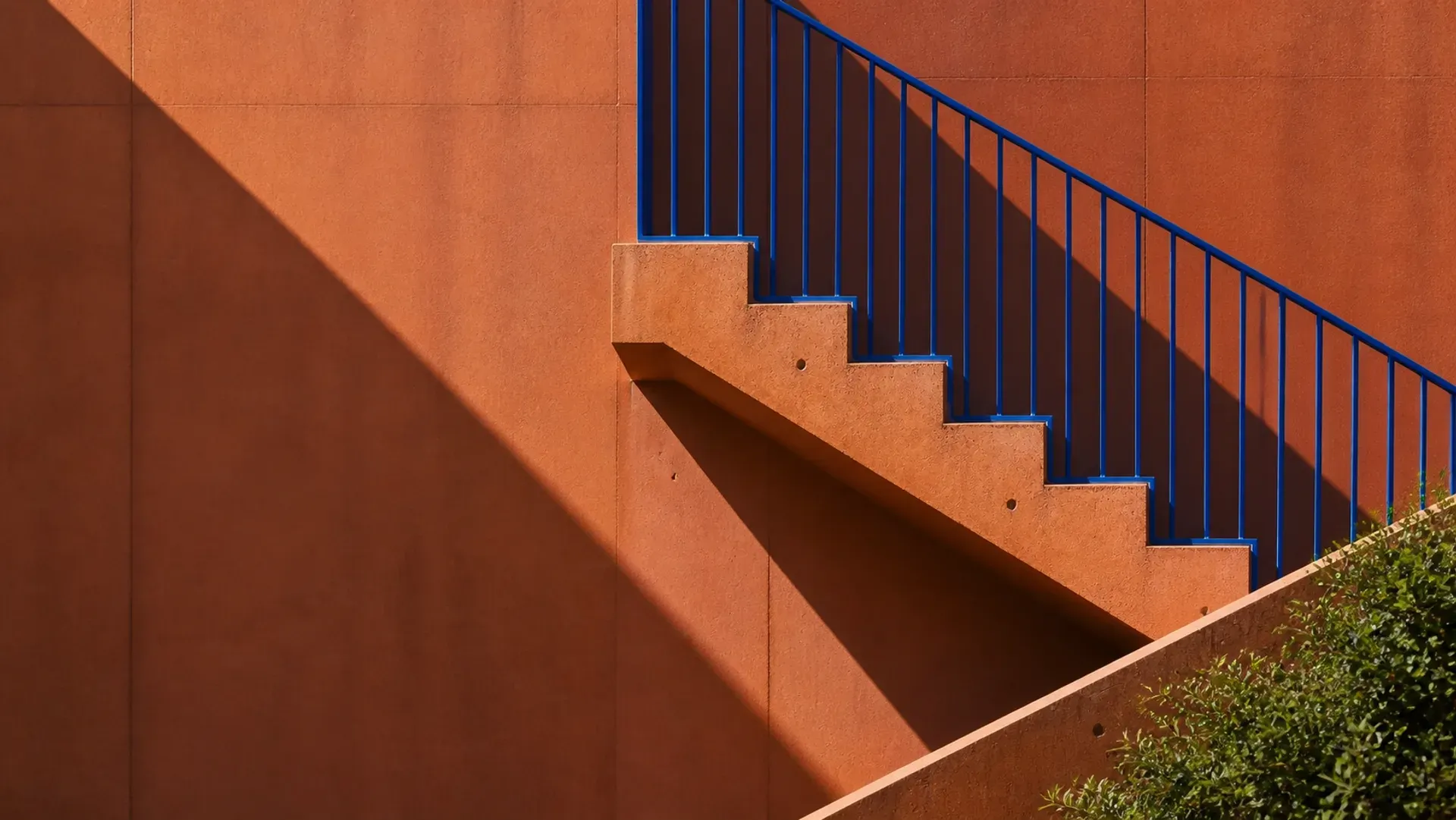 An exterior stair with a cobalt rail climbing a terracotta wall