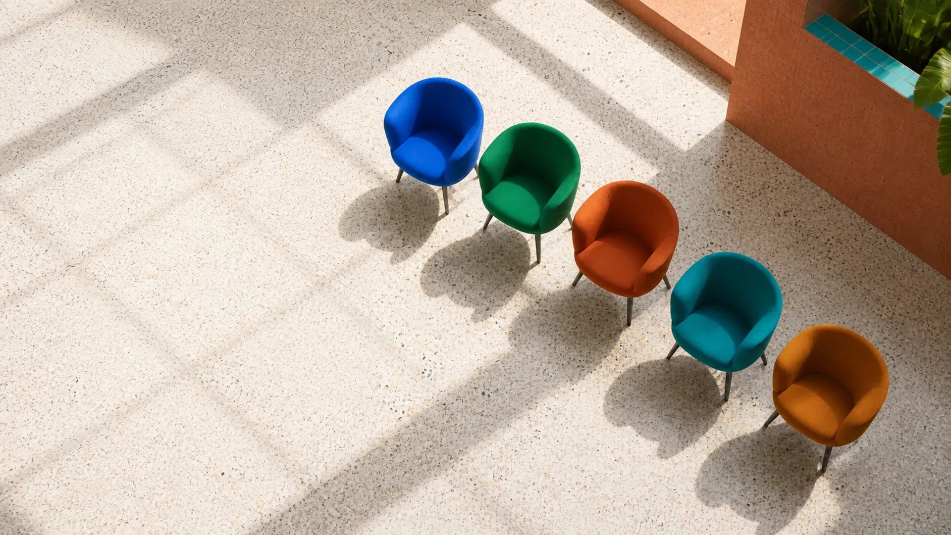 Five chairs in different colours arranged in a sunlit courtyard, one seat waiting to be filled