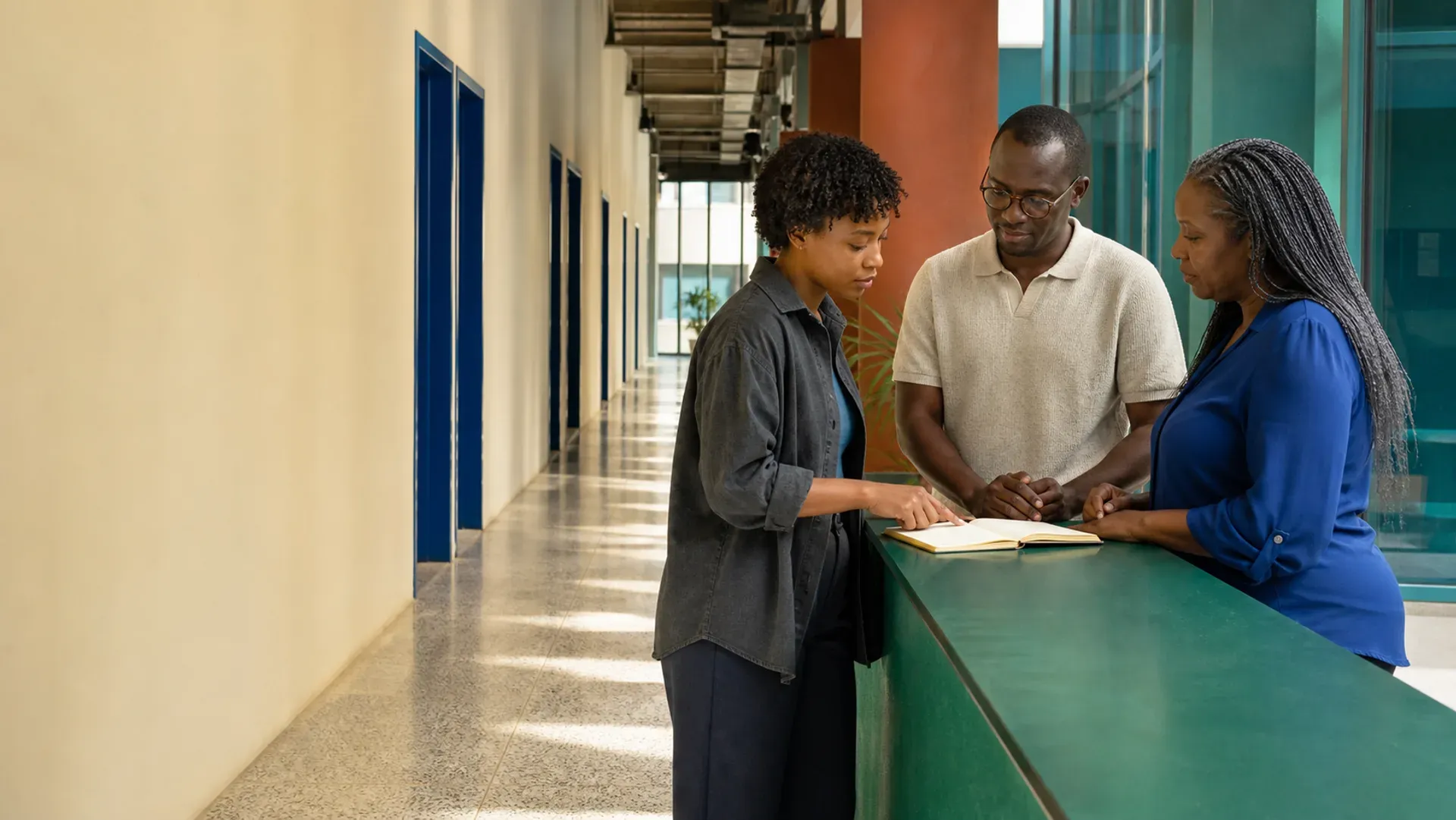Three colleagues completing a handover at a green counter in a daylit corridor