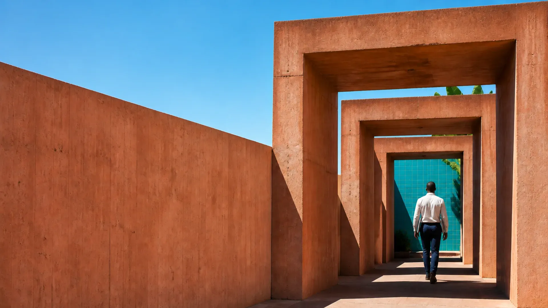A professional walking through a series of terracotta portals toward a teal doorway in hard sunlight